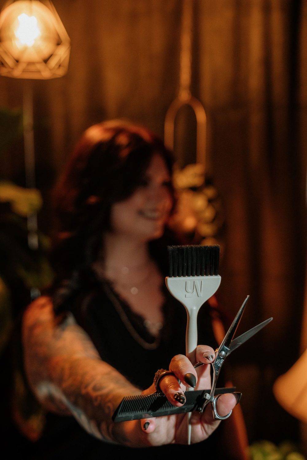 Color brush and shears held toward the camera in warm salon light